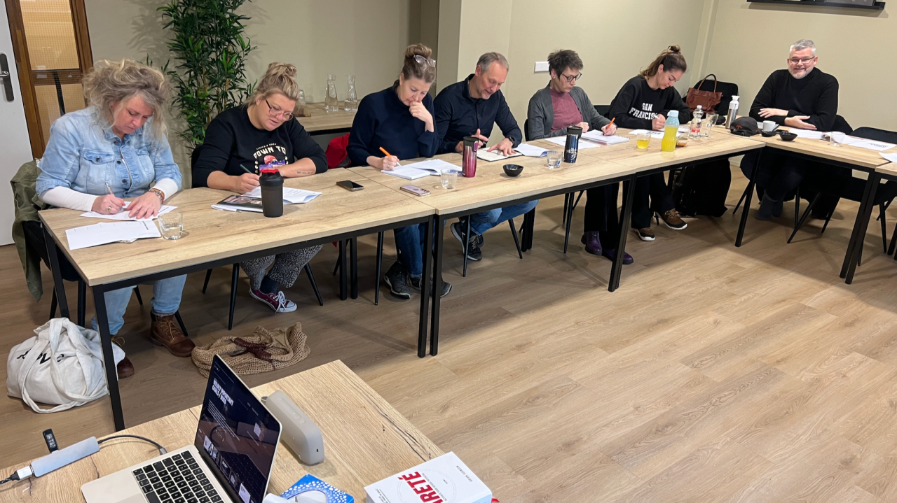 7 mensen die aan een groot bureau formulieren invullen tijdens de workshop